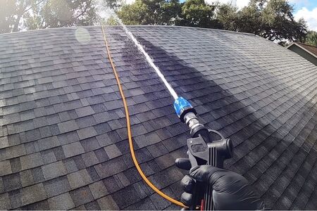 Soft wash gun shooting chemical onto shingle roof cleaning