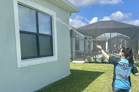 Woman in Blue shirt soft washing exterior of home