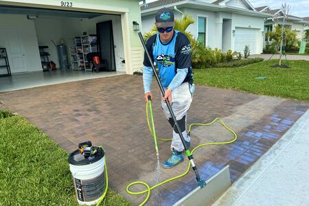 Man with blue shirt spraying sealer on brick paver driveway